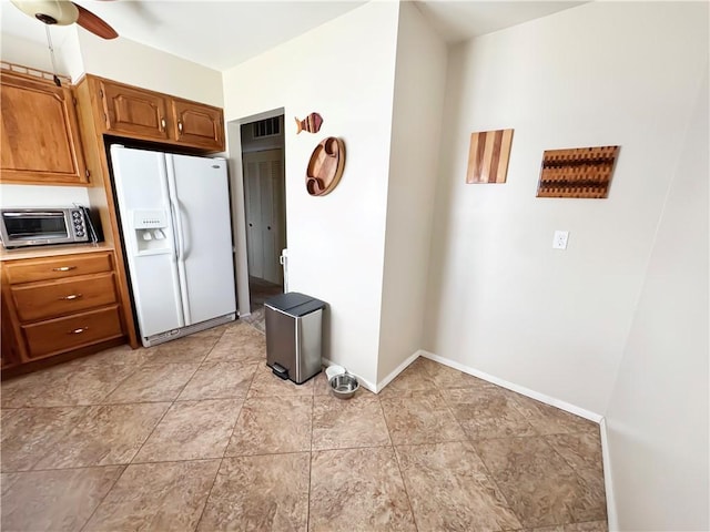 kitchen featuring brown cabinets, a ceiling fan, white fridge with ice dispenser, a toaster, and baseboards