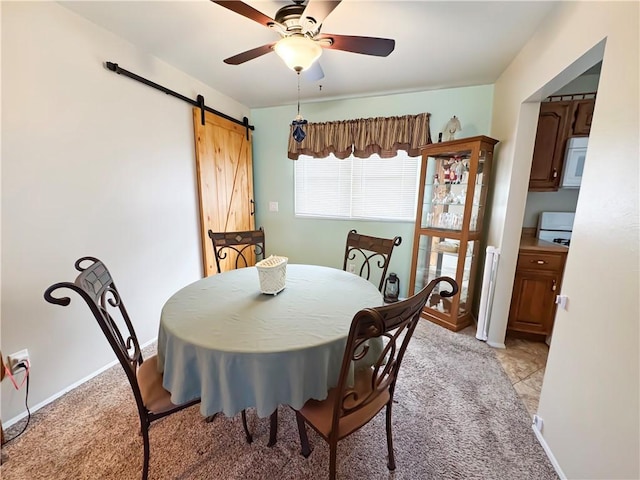 dining space featuring baseboards, light colored carpet, a ceiling fan, and a barn door