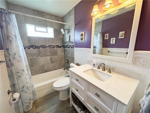 full bathroom featuring vanity, wood finished floors, shower / bathtub combination with curtain, a wainscoted wall, and toilet