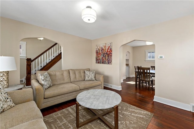 living room featuring baseboards, arched walkways, wood finished floors, and stairs