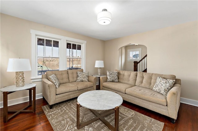 living room featuring dark wood-type flooring, a healthy amount of sunlight, arched walkways, and baseboards