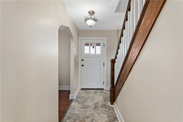 entryway with stone finish flooring, baseboards, arched walkways, and stairway