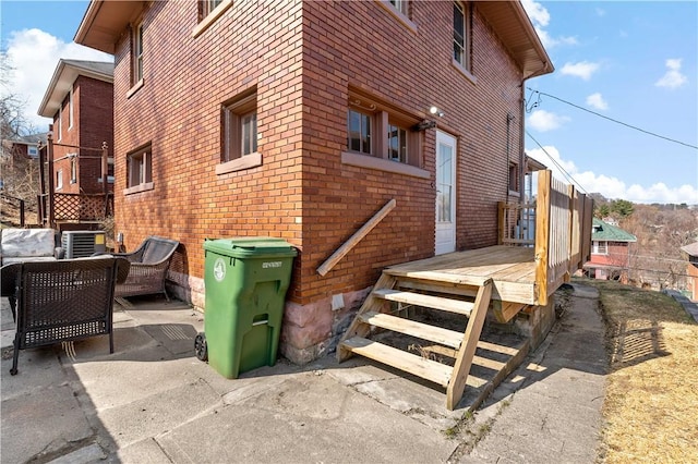 view of property exterior featuring a patio, brick siding, and a wooden deck