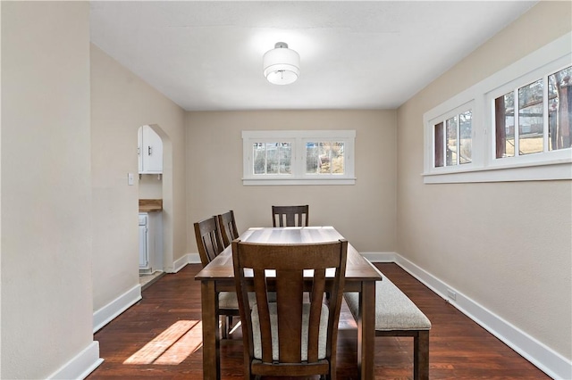 dining space featuring arched walkways, baseboards, dark wood-type flooring, and plenty of natural light