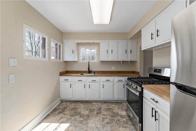 kitchen with baseboards, appliances with stainless steel finishes, stone finish floor, white cabinetry, and a sink