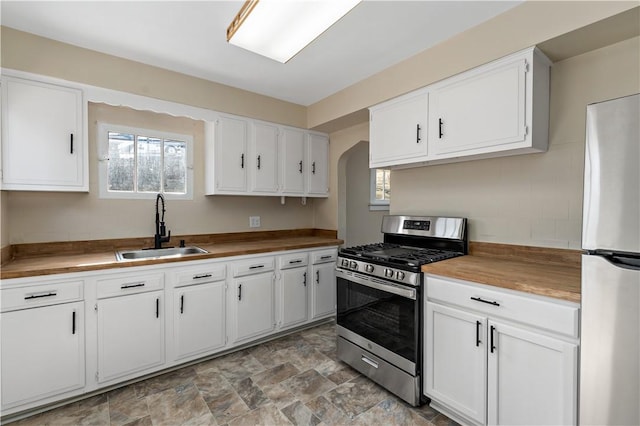 kitchen with arched walkways, a sink, stainless steel appliances, white cabinets, and wood counters