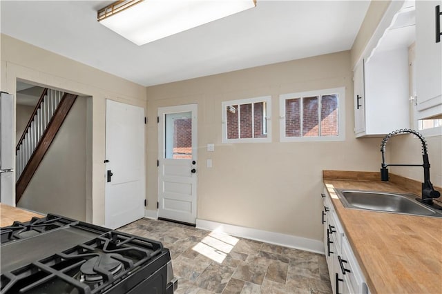 kitchen featuring black gas stove, butcher block countertops, stone finish floor, white cabinetry, and a sink