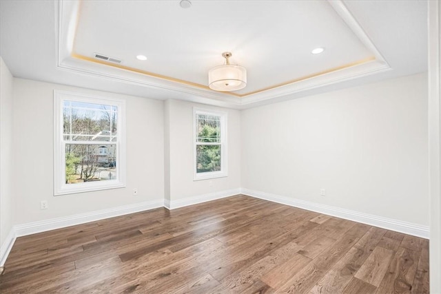 unfurnished room with a tray ceiling, baseboards, visible vents, and wood finished floors