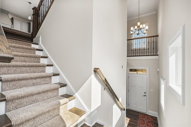 staircase with wood finished floors, a high ceiling, an inviting chandelier, crown molding, and baseboards