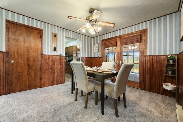 dining room featuring a wainscoted wall, wallpapered walls, carpet, and a ceiling fan