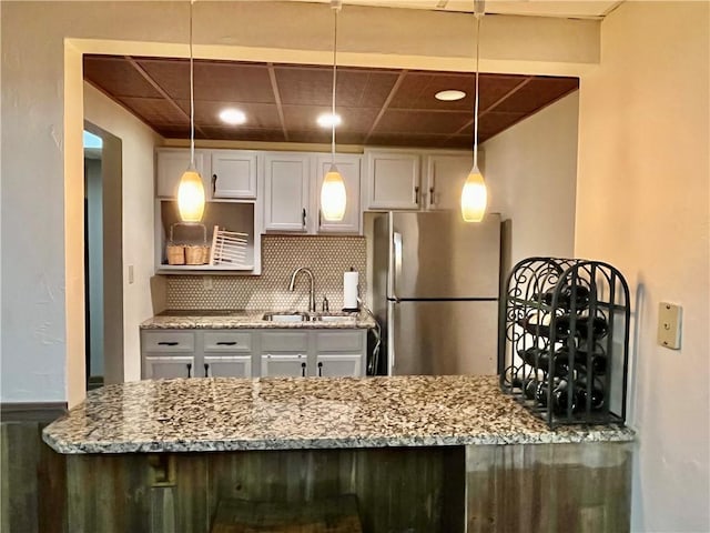 kitchen with backsplash, light stone counters, freestanding refrigerator, white cabinetry, and a sink