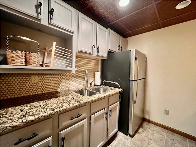 kitchen with tasteful backsplash, baseboards, light stone countertops, white cabinets, and a sink