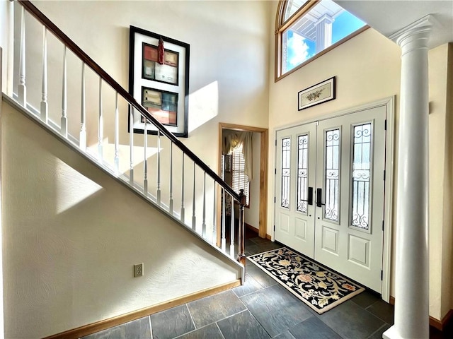 foyer with baseboards, a high ceiling, stairs, and ornate columns