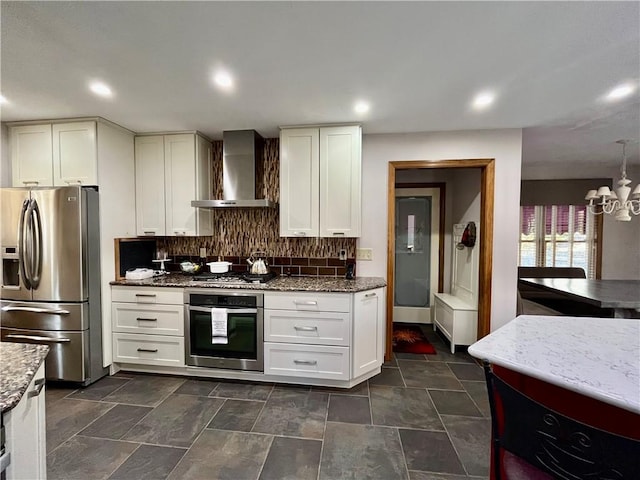 kitchen featuring tasteful backsplash, stainless steel appliances, an inviting chandelier, white cabinetry, and wall chimney exhaust hood