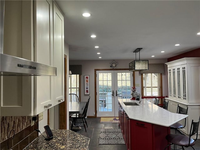 kitchen featuring wall chimney range hood, stone tile floors, recessed lighting, french doors, and a sink