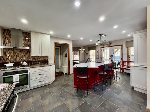 kitchen featuring white cabinetry, wall chimney exhaust hood, backsplash, and stainless steel appliances