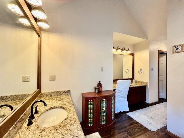 bathroom featuring wood finished floors, two vanities, lofted ceiling, and a sink