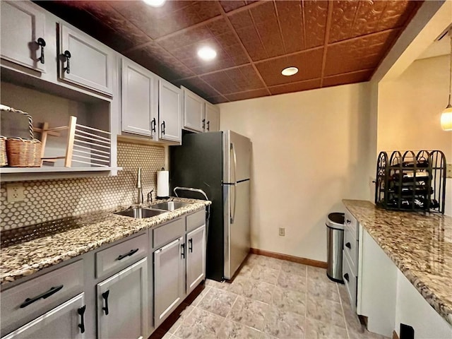 kitchen featuring baseboards, light stone countertops, decorative backsplash, freestanding refrigerator, and a sink