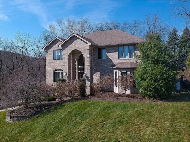 traditional-style house featuring brick siding, a front yard, and a shingled roof