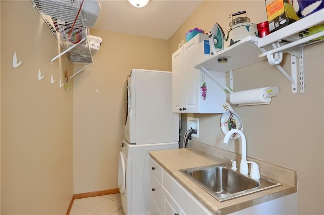 washroom with baseboards, light tile patterned flooring, cabinet space, a sink, and stacked washer / dryer