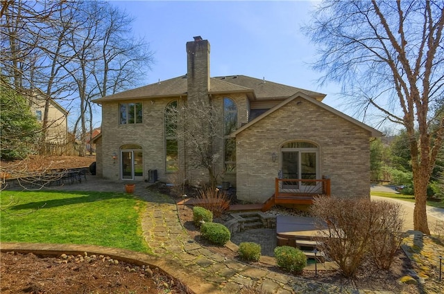 rear view of house featuring a lawn, a shingled roof, brick siding, a chimney, and a patio area