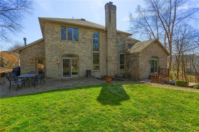 rear view of house with a patio, a lawn, a chimney, and brick siding