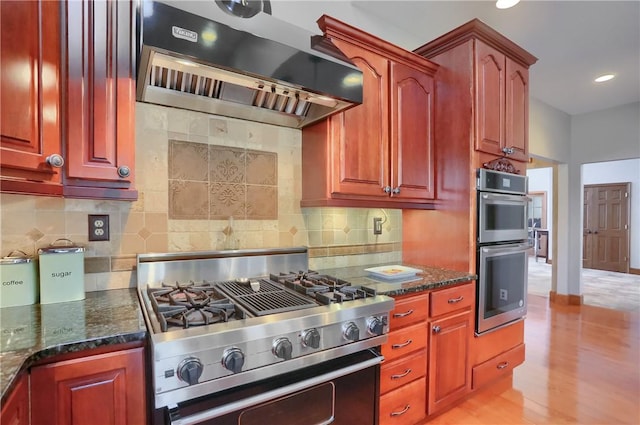 kitchen featuring dark stone counters, range with gas stovetop, extractor fan, and double oven