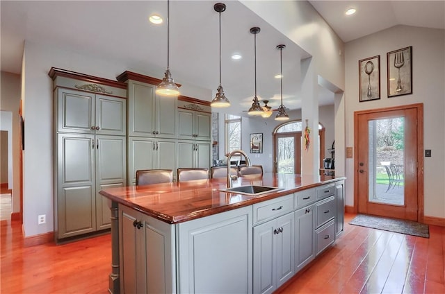 kitchen featuring a sink, decorative light fixtures, a kitchen island with sink, and light wood finished floors