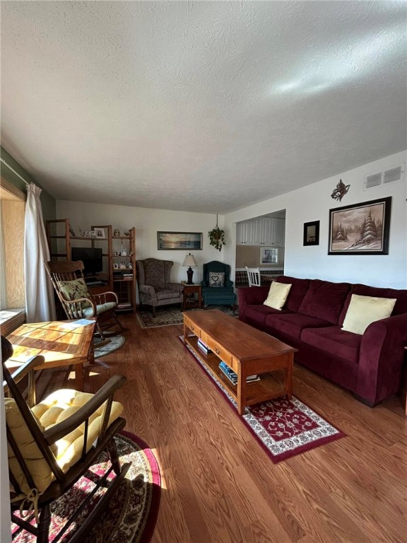 living room with visible vents, a textured ceiling, and wood finished floors