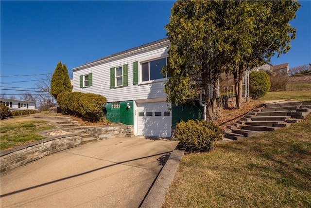 view of side of property with stairway, an attached garage, concrete driveway, and a yard