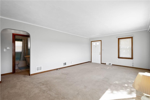 unfurnished living room featuring arched walkways, visible vents, ornamental molding, and carpet floors