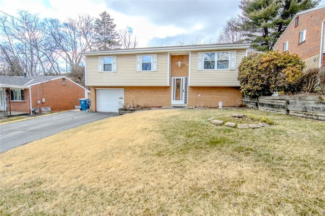 split foyer home with aphalt driveway, a garage, brick siding, and a front yard