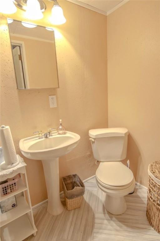 half bathroom with crown molding, toilet, and baseboards