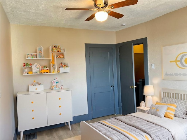 bedroom with visible vents, light wood-style flooring, a textured ceiling, and ceiling fan