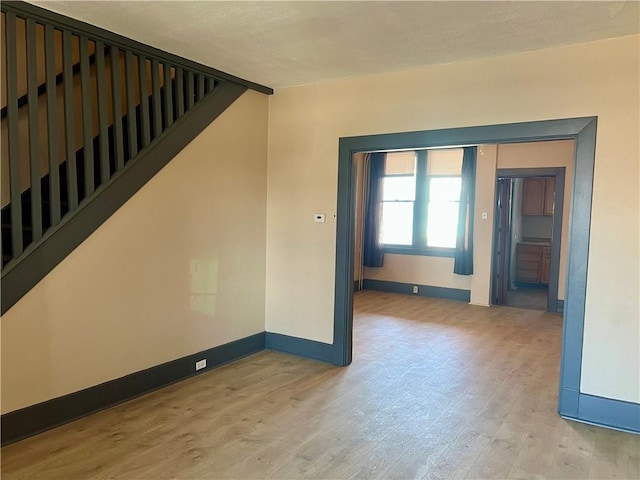 empty room featuring stairs, baseboards, and wood finished floors