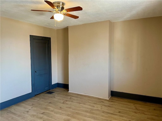 spare room featuring baseboards, light wood-style floors, ceiling fan, and a textured ceiling