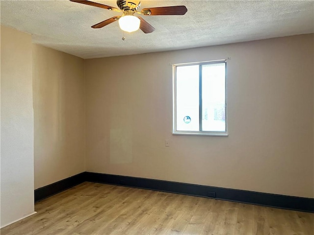 spare room with light wood-type flooring, baseboards, and a textured ceiling