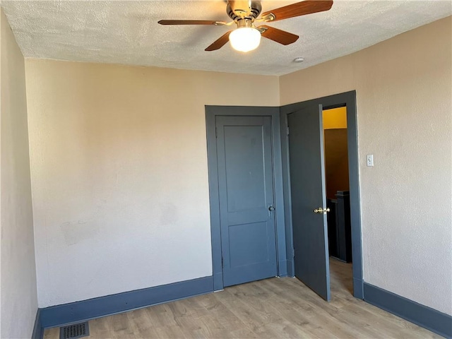 spare room featuring visible vents, baseboards, light wood-style floors, a textured ceiling, and a ceiling fan