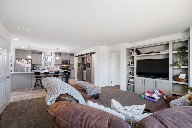 living area with a barn door, recessed lighting, and light carpet