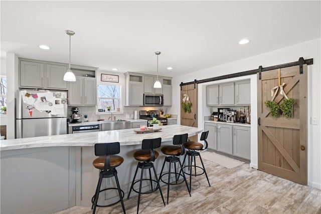 kitchen featuring gray cabinetry, a barn door, a kitchen breakfast bar, appliances with stainless steel finishes, and a sink