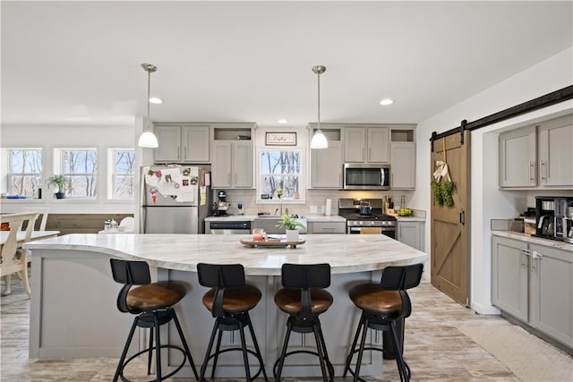 kitchen with a breakfast bar area, gray cabinets, decorative backsplash, appliances with stainless steel finishes, and a barn door