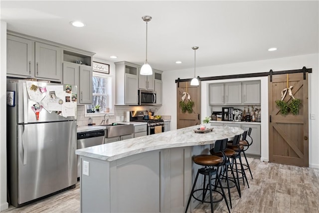 kitchen featuring a barn door, a center island, appliances with stainless steel finishes, and gray cabinetry