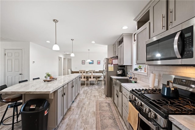 kitchen featuring gray cabinetry, a kitchen island, a kitchen bar, light wood-style flooring, and stainless steel appliances