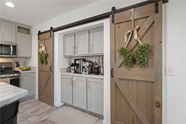 kitchen with gray cabinetry, light countertops, a barn door, light wood-style flooring, and stainless steel appliances