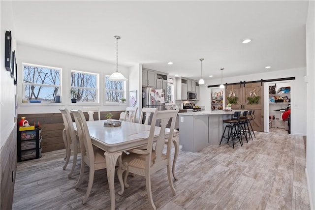 dining space with light wood finished floors, recessed lighting, and a barn door
