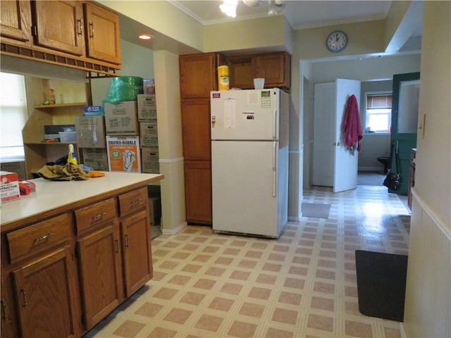 kitchen featuring light floors, light countertops, ornamental molding, brown cabinets, and freestanding refrigerator