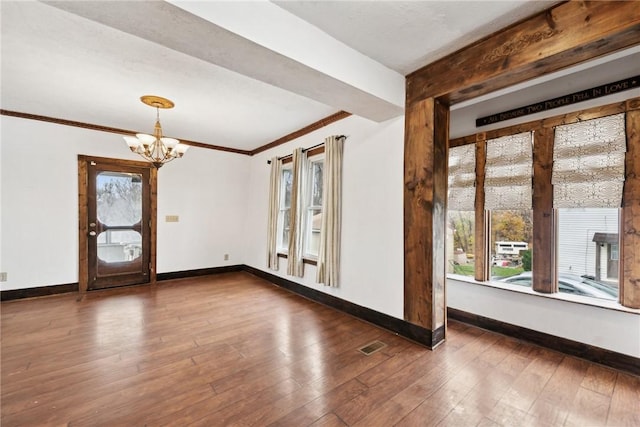 spare room featuring visible vents, ornamental molding, hardwood / wood-style floors, an inviting chandelier, and baseboards