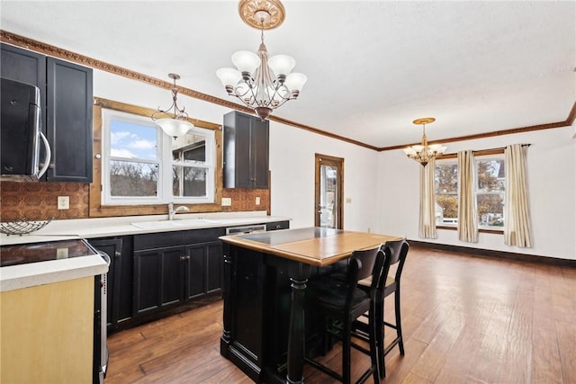 kitchen featuring a sink, stainless steel microwave, dark cabinets, a healthy amount of sunlight, and a chandelier