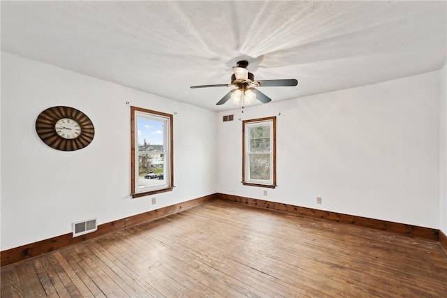 spare room featuring visible vents, a healthy amount of sunlight, ceiling fan, and hardwood / wood-style flooring