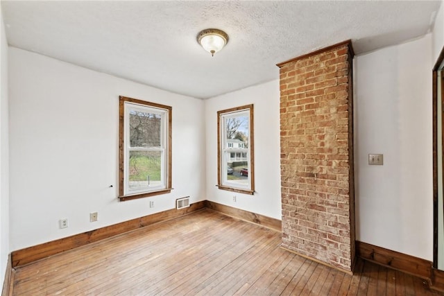 spare room with baseboards, wood-type flooring, a textured ceiling, and visible vents